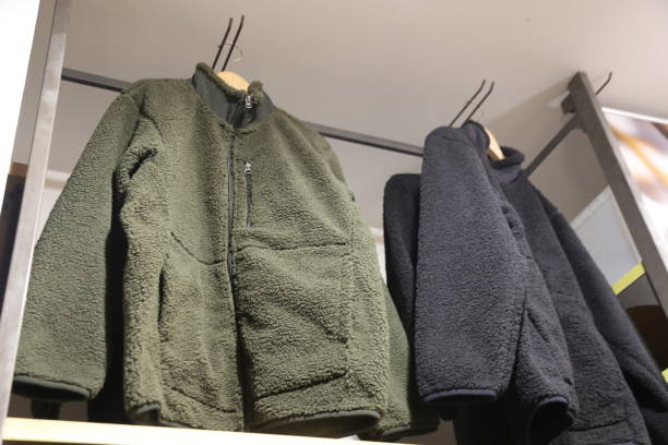 Two jackets hanging on a rack, one green and one black. The green jacket has a zipper pocket and a hood